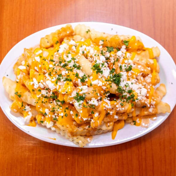 Crinkle-cut fries topped with melted cheese, crumbled feta, and chopped parsley on a white plate.