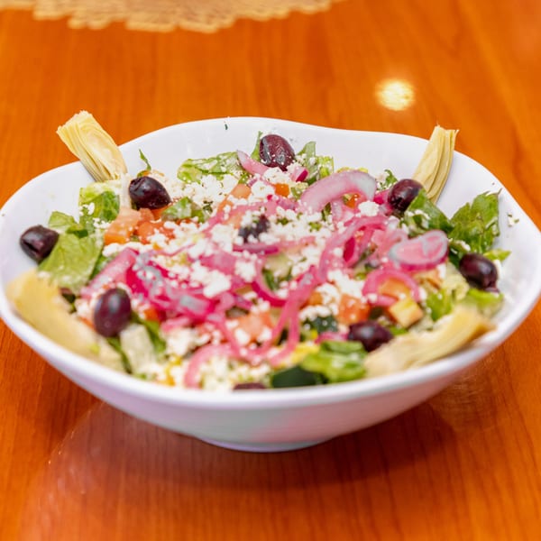 A vibrant Greek salad in a white bowl, featuring lettuce, feta, olives, red onions, and artichoke hearts.