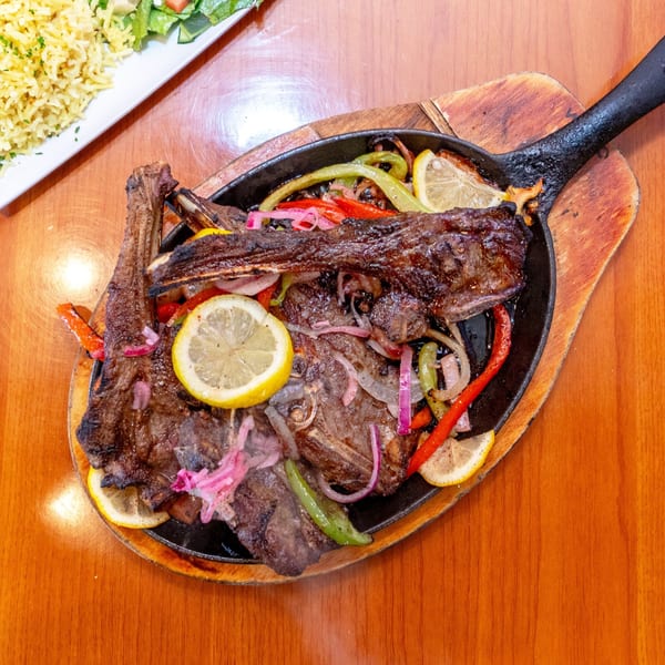 Grilled lamb chops with colorful bell peppers, red onions, and lemon slices in a sizzling skillet.