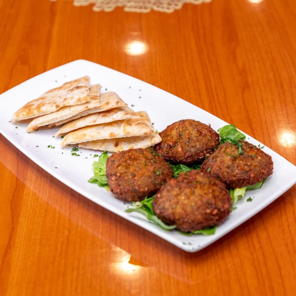 Four falafel patties on lettuce with pita bread triangles on a white rectangular plate.