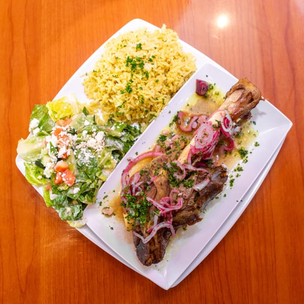 Lamb shank with pickled red onions, rice pilaf, and a side salad with feta cheese.