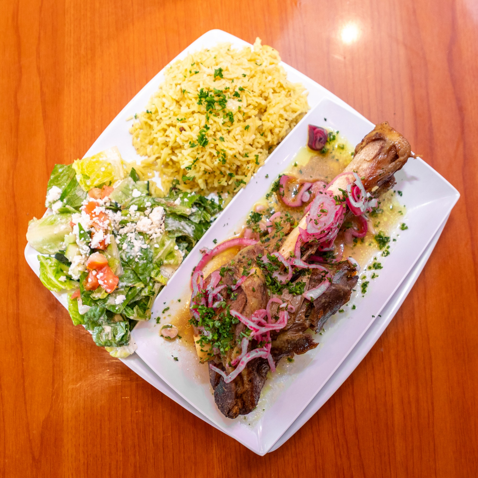Lamb shank with pickled red onions, rice pilaf, and a side salad with feta cheese.