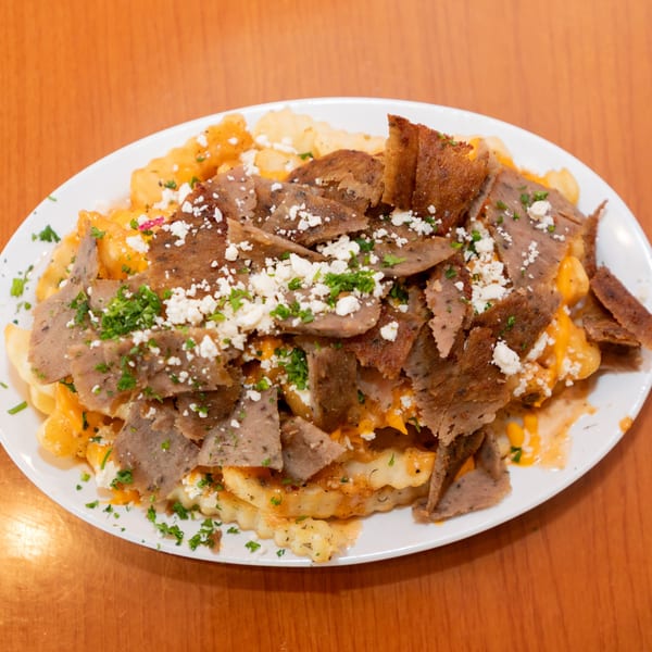 A white plate piled high with golden french fries, topped with gyro meat, feta cheese, and parsley.