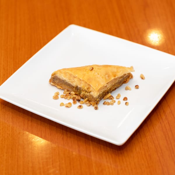 A triangular piece of baklava with chopped nuts on a white square plate.