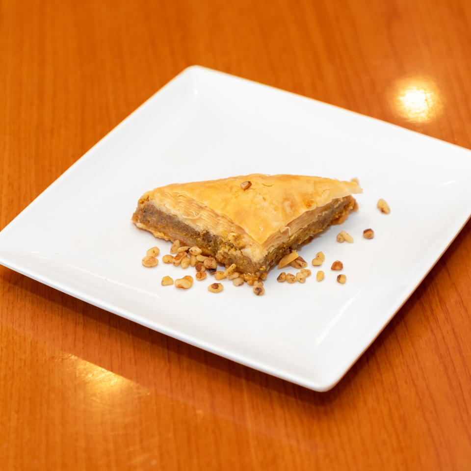 A triangular piece of baklava with chopped nuts on a white square plate.
